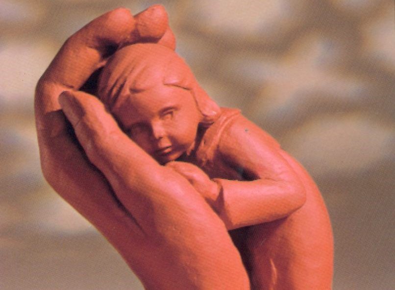 Ton-Figur: eine Hand hält tröstend ein Kind.