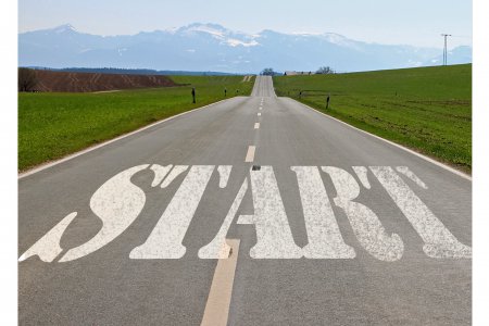 Das Wort &quot;Start&quot; steht auf einer Straße, die geradeaus führt. Die Landschaft ich hügelig, im Hintergrund sind Berge zu sehen.