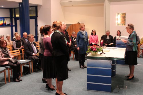 Hinter dem Altar steht Inge Troch und liest den vor dem Altar stehenden evangelischen Absolventen die Beauftragung vor.