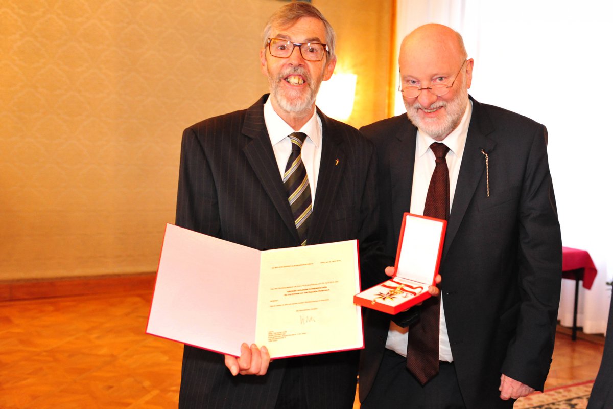 Superintendent Hansjörg Lein hält die Urkunde und das Ehrenkreuz in der Hand, neben ihm steht Ministerialrat Karl Schwarz.